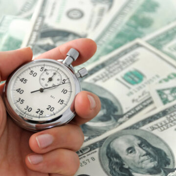 Human hand keeping a stop-watch against dollar bank note